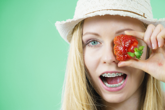A girl with braces holding up a strawberry to her eye