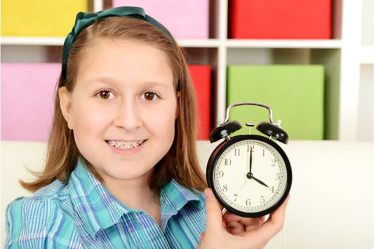 A girl with metal braces holding a clock