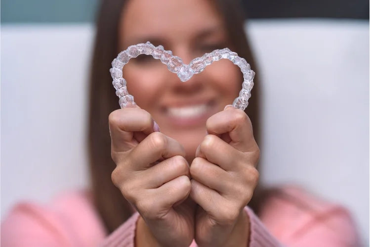 A woman holding clear aligners in her hands to make a heart shape
