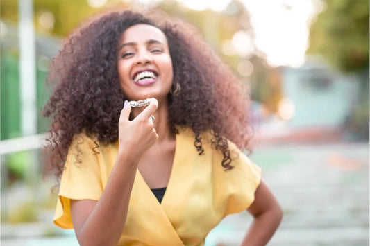 A woman smiling and holding a pair of aligners