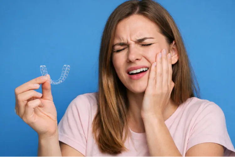  A girl holding retainers and holding her jaw in pain 